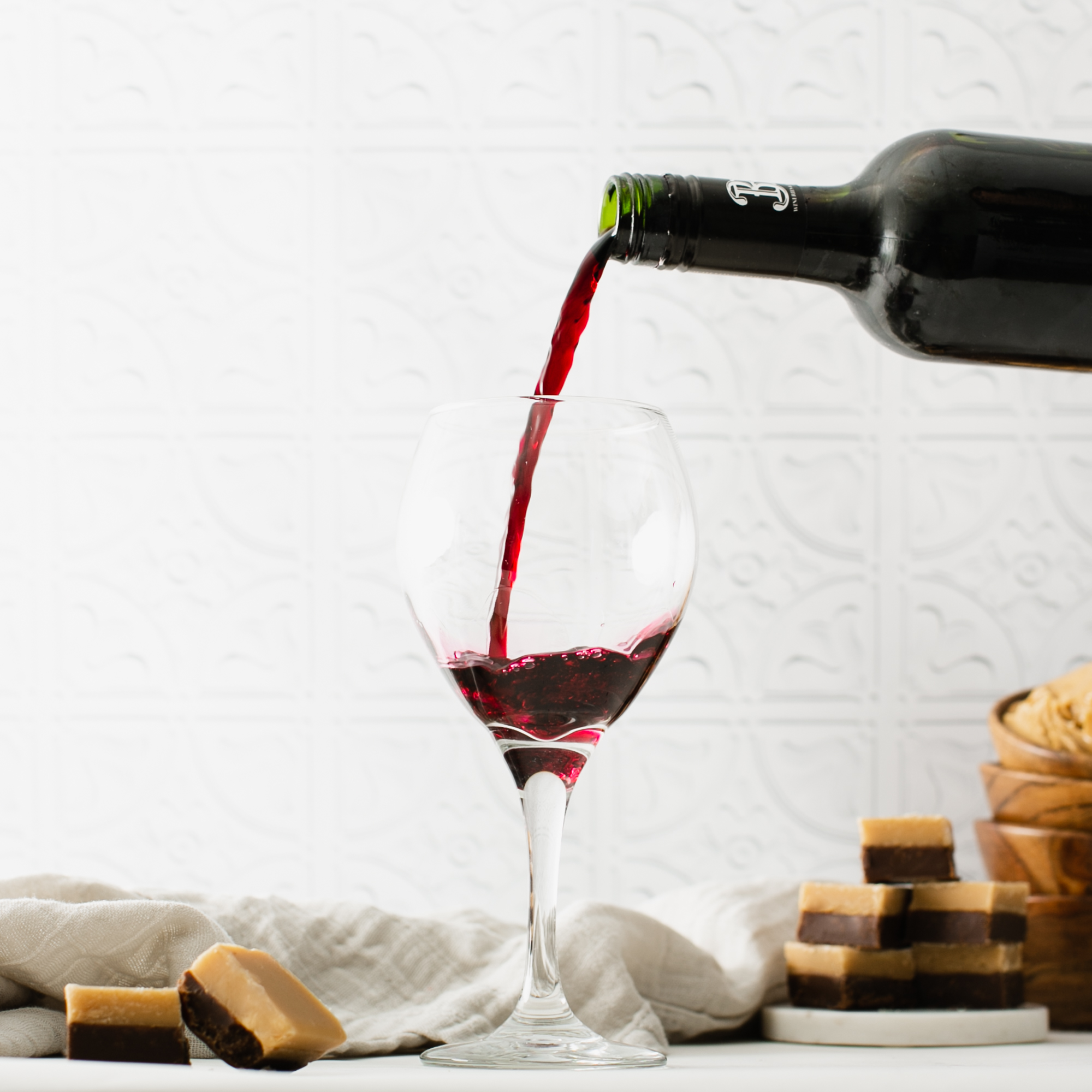 red wine pouring into wine glass surrounded by chocolate peanut butter layered fudge